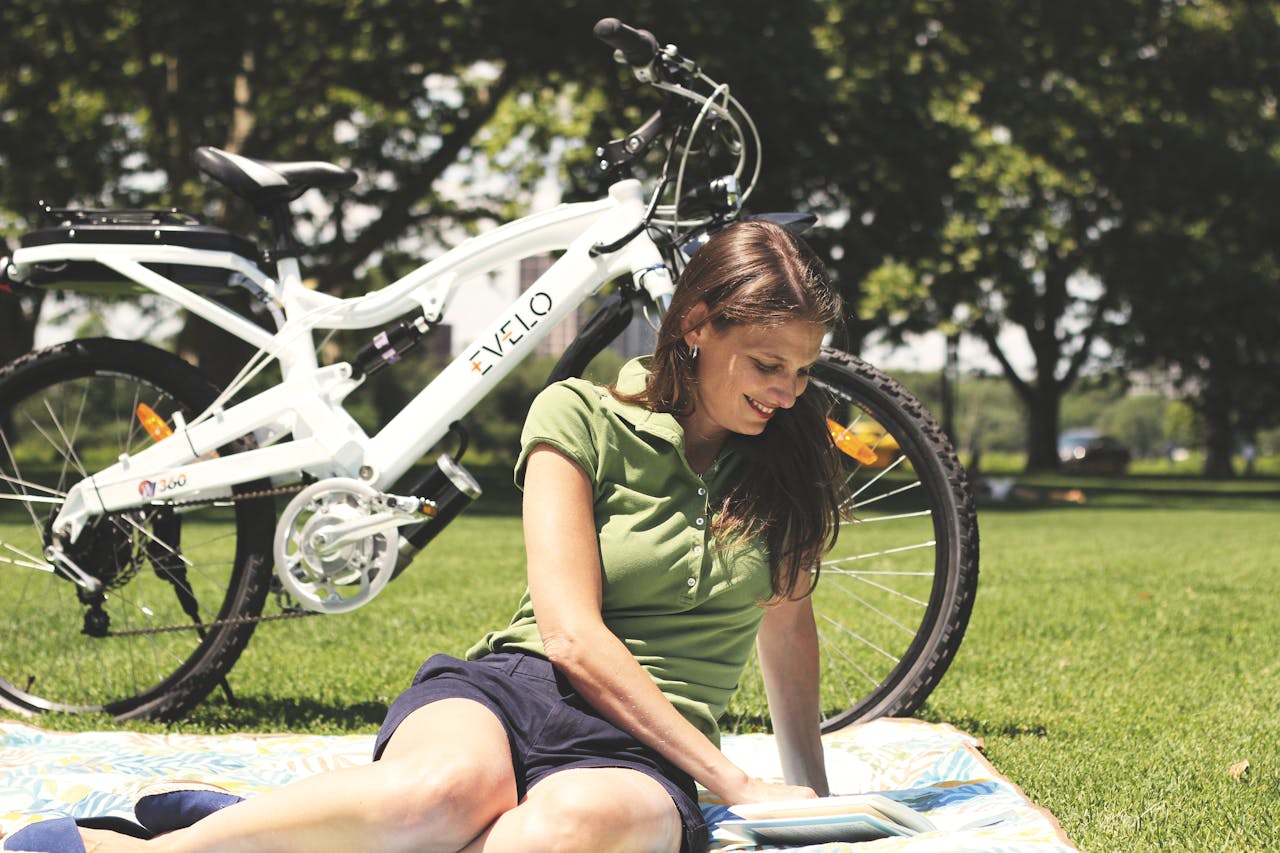 Mastering the First Impression: Your intriguing post title goes here A woman enjoys leisure time on a picnic blanket beside an electric bike in a sunny park.